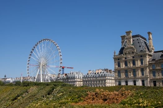 A sunny day view of a Ferris wheel near a historic building in Paris, France.